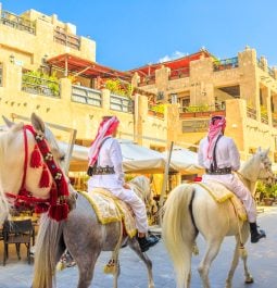heritage police officers in traditional 1940s Qatari uniform at old Souq Waqif riding white Arabian Horses
