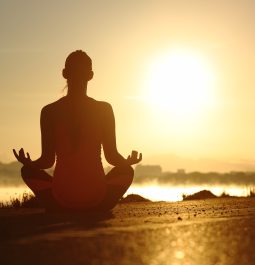 Silhouette of a fitness woman exercising yoga meditation exercises with the sun in the background