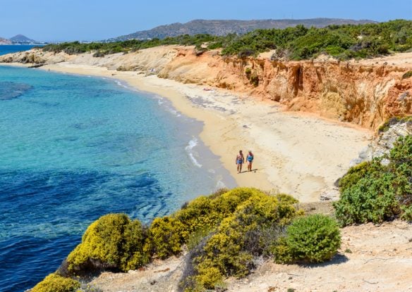 beach with dunes and crystal-clear water and couple walking on beach